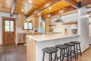 A modern kitchen with wooden beams, a large island with bar stools, stainless steel appliances, and a white tiled backsplash.