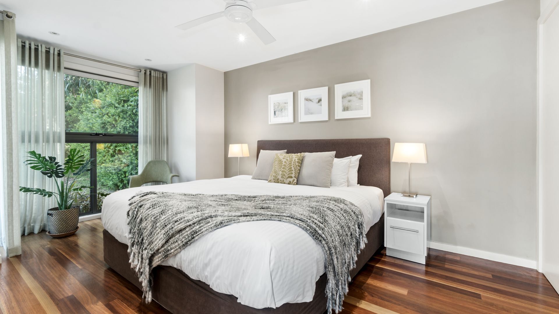 Ein modernes Schlafzimmer mit einem großen Bett, einem Deckenventilator, einem Fenster mit Vorhängen und einem Blumentopf.