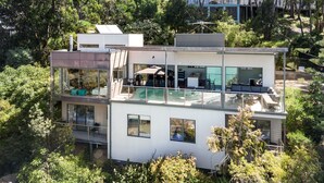 Een modern meerlaags huis met een glazen balkon, buitenmeubels en een zwembad.