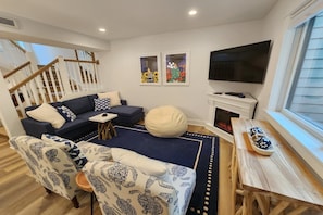Uma sala de estar com sofá, cadeiras, mesa de centro, televisão e obras de arte na parede.