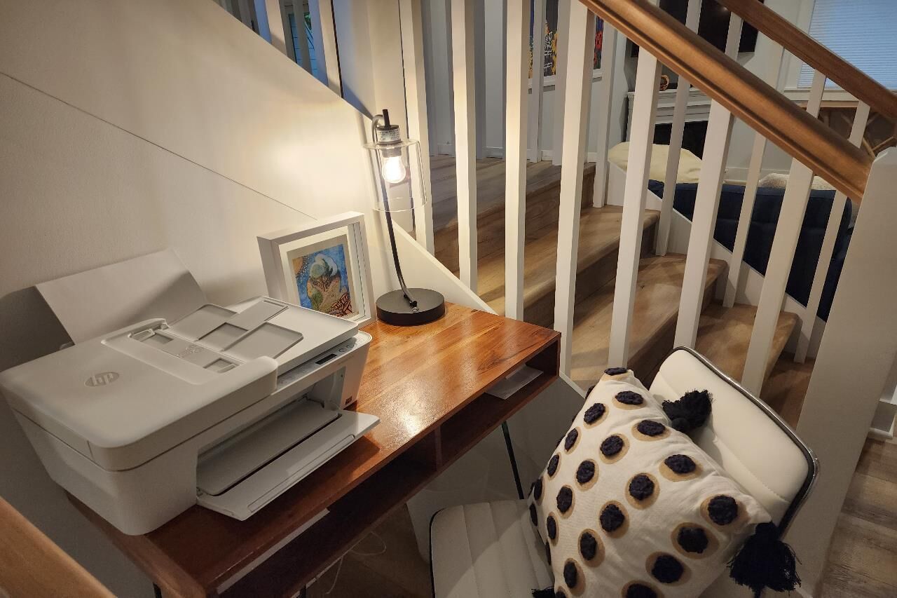 Ein Home-Office-Bereich mit Drucker, Lampe und einem Stuhl mit Sitzkissen in Punkteoptik.