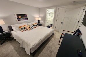 Quarto de hotel com cama, mesas de cabeceira, escrivaninha e espelho.