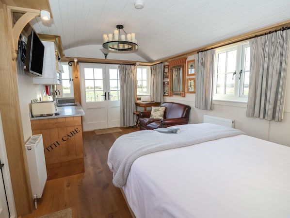 A bedroom with a large bed, wooden floor, a wooden cabinet labeled "THE CARE", a leather chair, a desk with a chair, and a window with curtains.