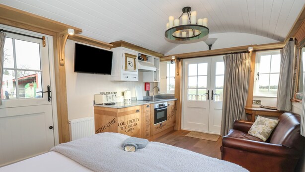 Ein gemütliches Zimmer mit einem Bett, einem Ledersofa, einer Küchenzeile und einem an der Wand befestigten Fernseher.