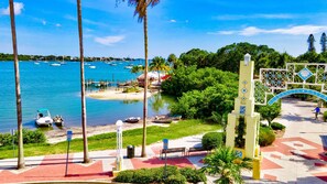 Stroll along the serene waterfront promenade with a clear view of the sea, surrounded by lush greenery and palm trees.