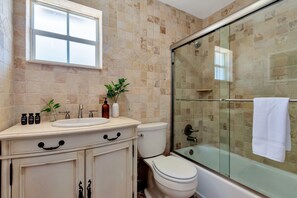 Une salle de bain avec une douche à parois de verre, des toilettes, un lavabo avec des articles de toilette et une fenêtre.