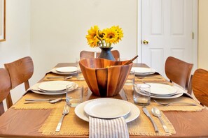 Une table à manger dressée avec des assiettes, des couverts et un saladier en bois rempli de tournesols.