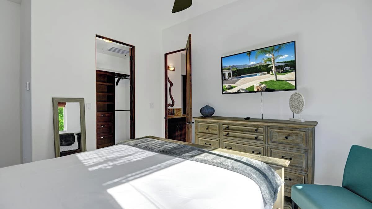 Quarto com cama, cômoda, televisão e pintura de paisagem.