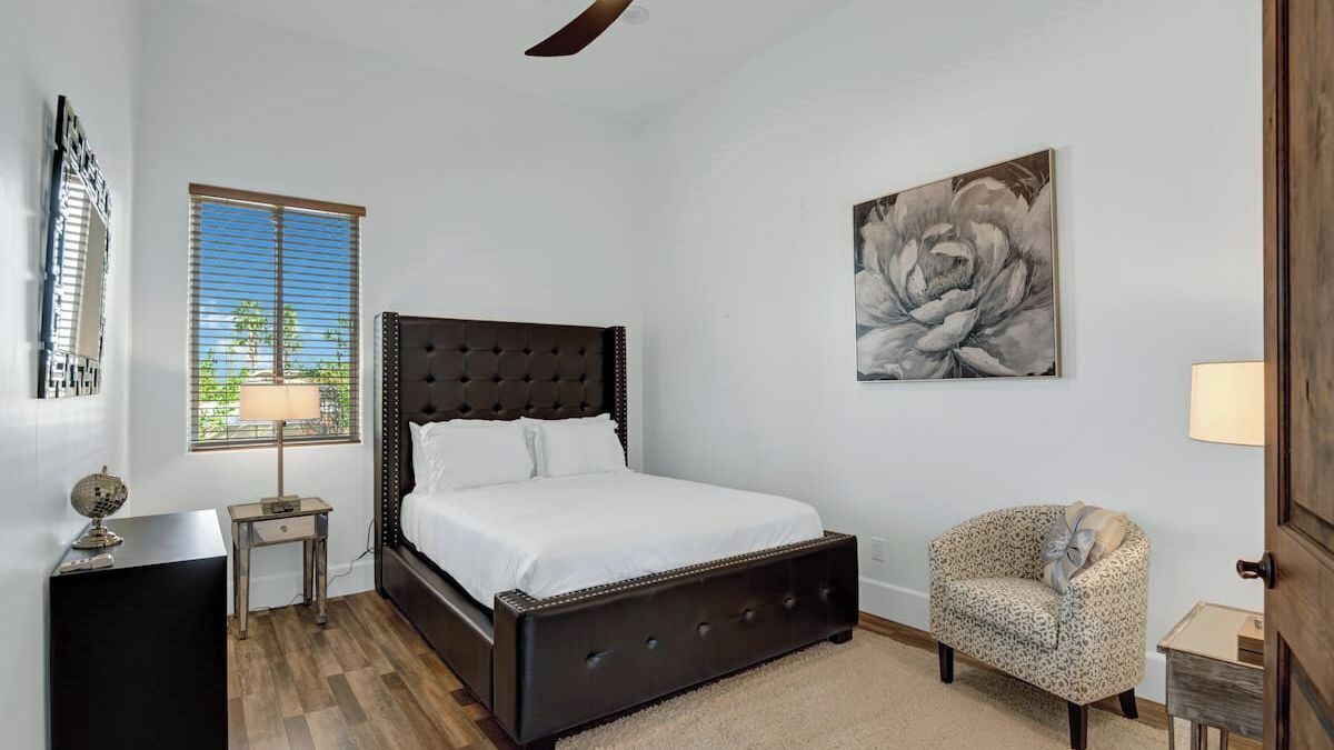 A bedroom with a bed, a chair, a desk, a lamp, and a painting on the wall.