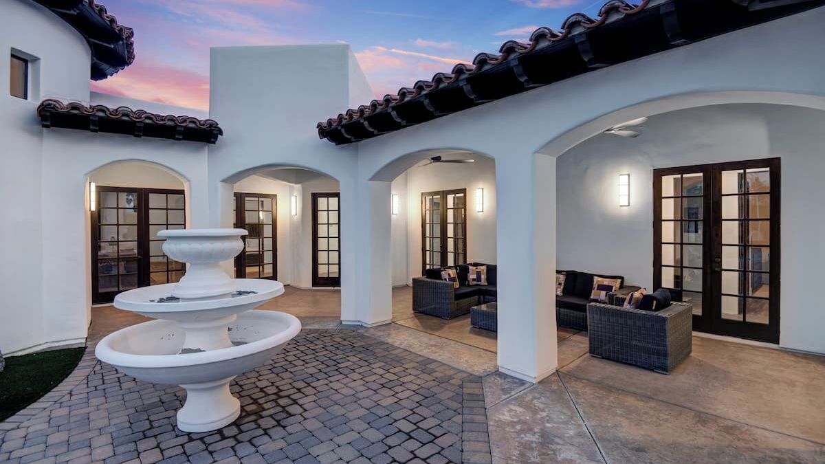 A courtyard with a white fountain, outdoor seating, and a tiled floor.