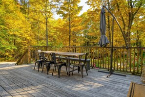 A wooden deck with a table and chairs, surrounded by a wooden fence and trees with yellow leaves.