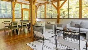 A spacious room with wooden beams, large windows, a dining area with chairs and a table, and a sofa with cushions. - Woodfall by Avantstay Tons of Outdoor Space (Monterey)