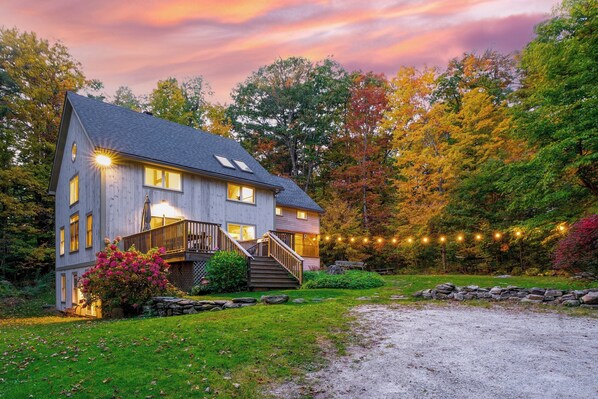A two-story house with a porch, a stone wall, and a gravel driveway.