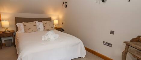 A neatly made bed with white linens and a folded towel, a wooden nightstand with a lamp, and a wooden chair.