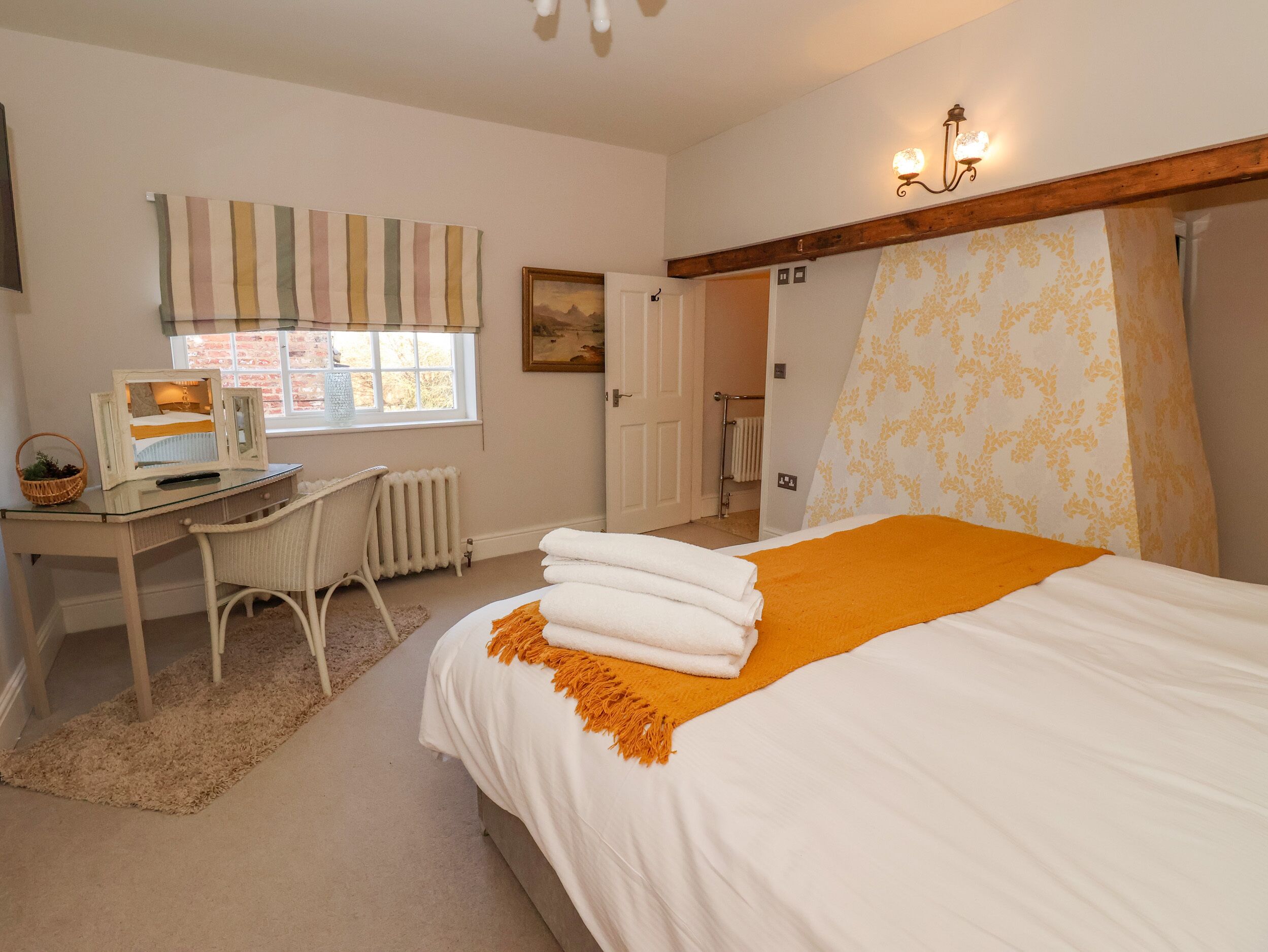 A bedroom with a bed, a desk, a chair, a radiator, a window, and a door.