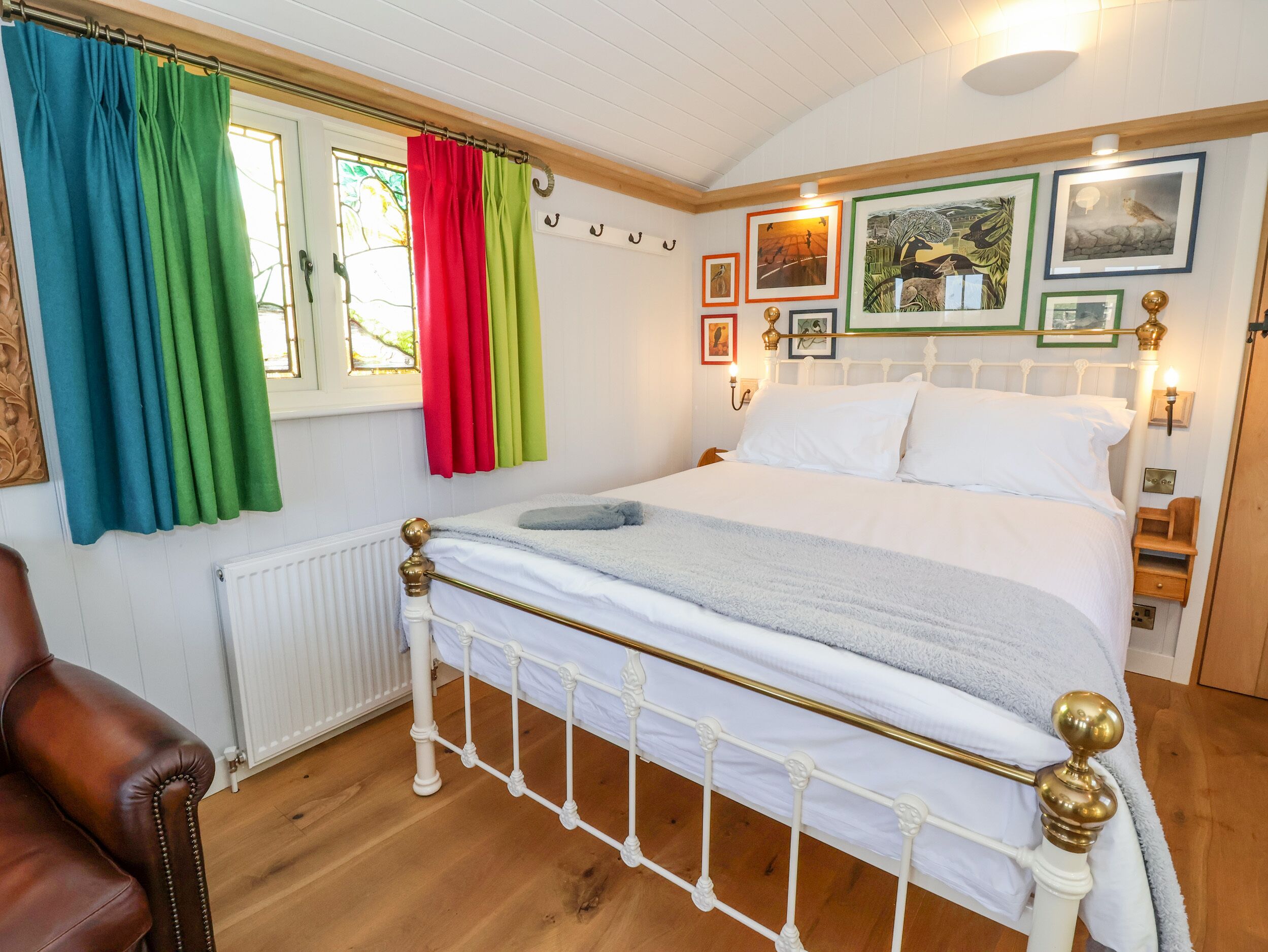 Une chambre à coucher bien rangée, avec un lit blanc, un plancher en bois et une fenêtre ornée de rideaux colorés.