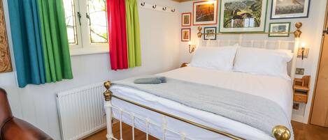 Une chambre à coucher bien rangée, avec un lit blanc, un plancher en bois et une fenêtre ornée de rideaux colorés.