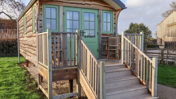 A wooden cabin with a curved roof, a wooden staircase, and a bench outside. - The Studio (York)
