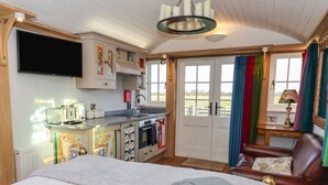 A cozy room with a bed, a desk, a chair, a TV, a kitchen area, and a window with curtains. - The Studio (York)