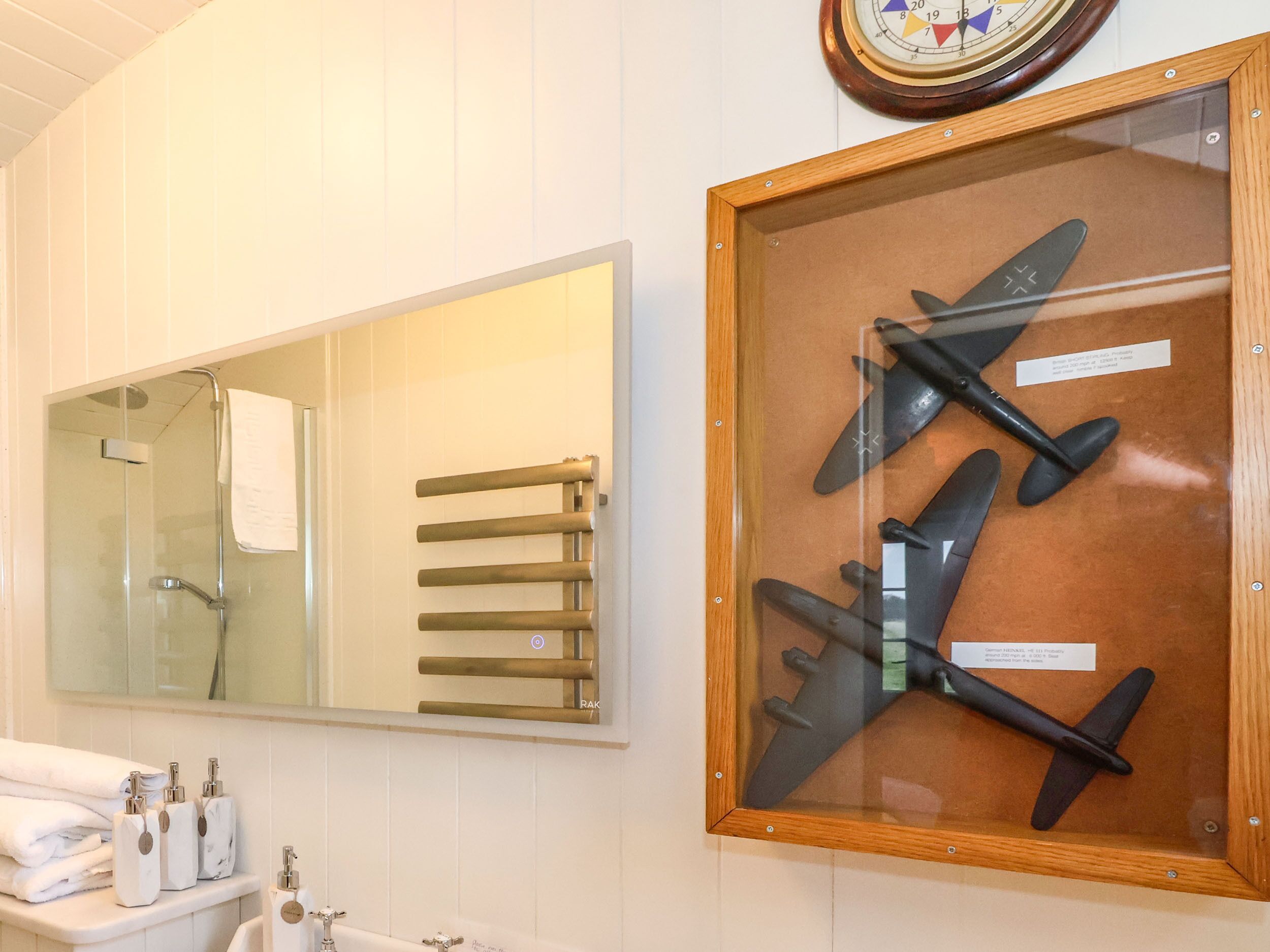 Un baño con espejo, toallero y un modelo de avión enmarcado.