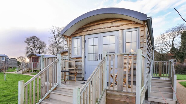 A wooden cabin with a curved roof, a front door, and a small porch with a chair and table.