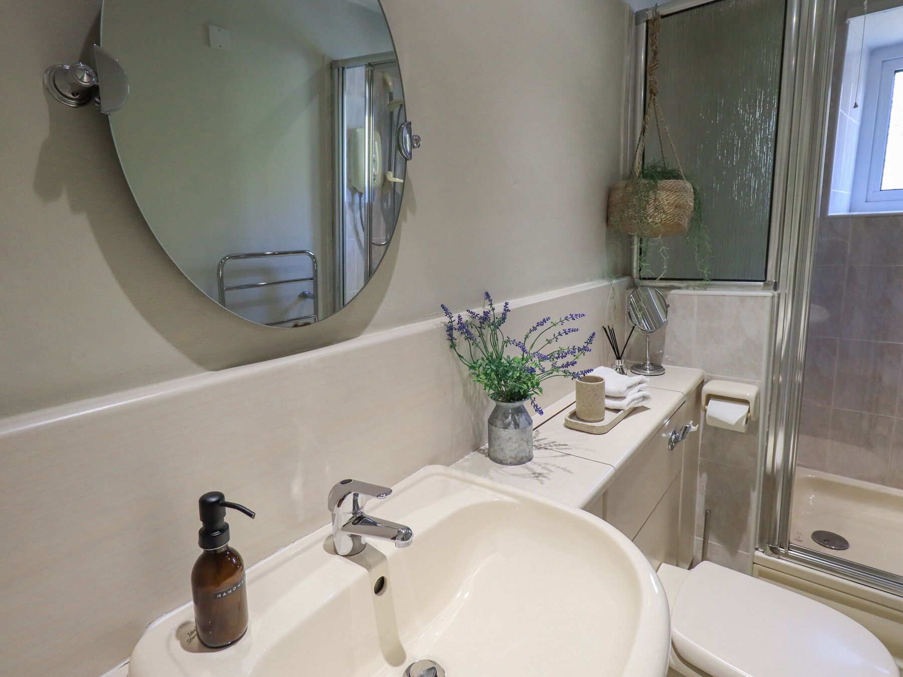 Ein Badezimmer mit großem Spiegel, Waschbecken mit Seifenspender, Toilette und Duschbereich.
