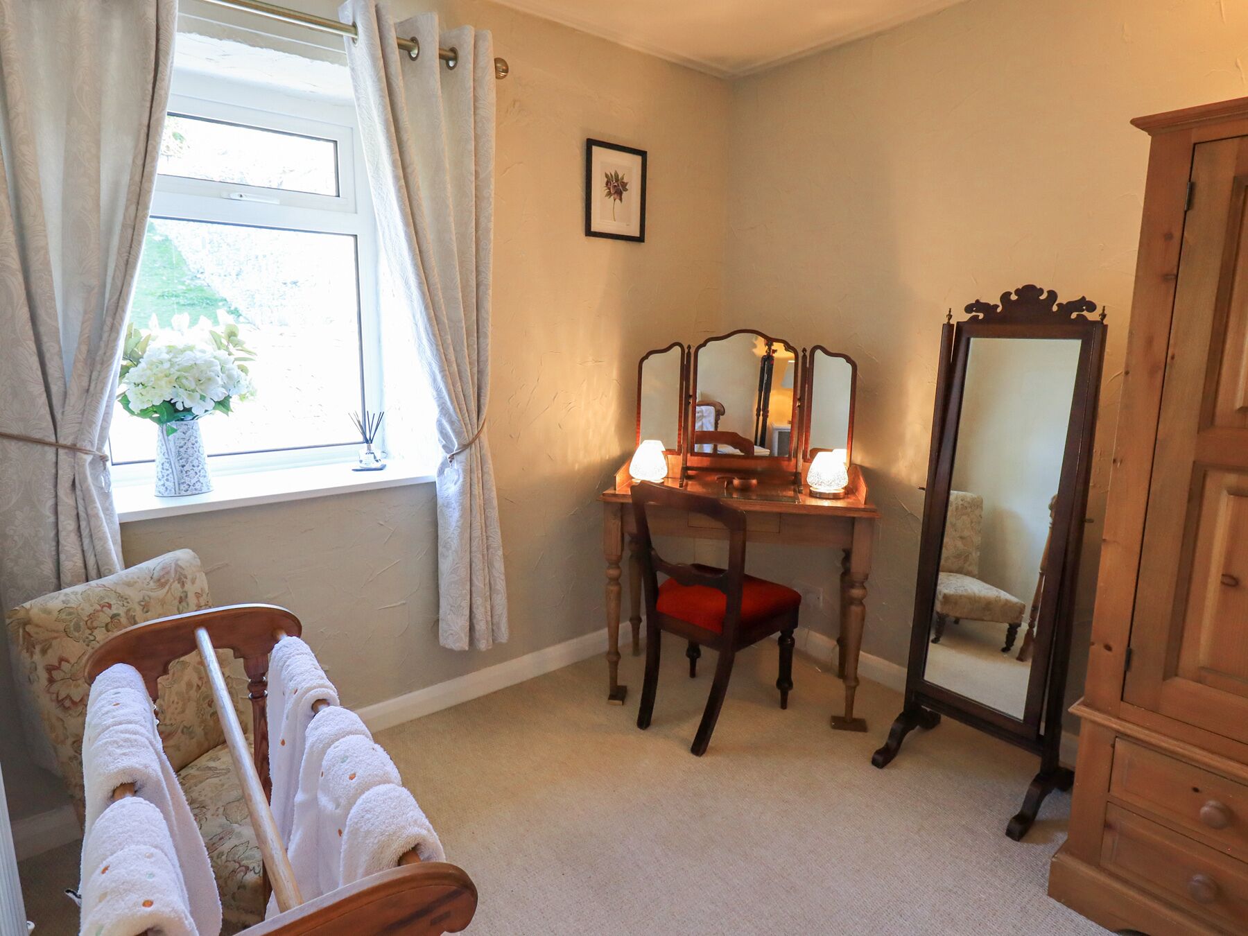 A bedroom with a bed, a vanity with a mirror, a dresser, and a window with curtains.