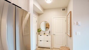 A hallway with a white door, a white cabinet with a mirror, and a woven stool. - Modern Condo w/AC, close to YYC (Calgary)