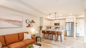A modern kitchen with a central island, wooden chairs, and stainless steel appliances. - Modern Condo w/AC, close to YYC (Calgary)