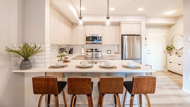 A modern kitchen with a central island, stainless steel appliances, and wooden bar stools. - Modern Condo w/AC, close to YYC (Calgary)