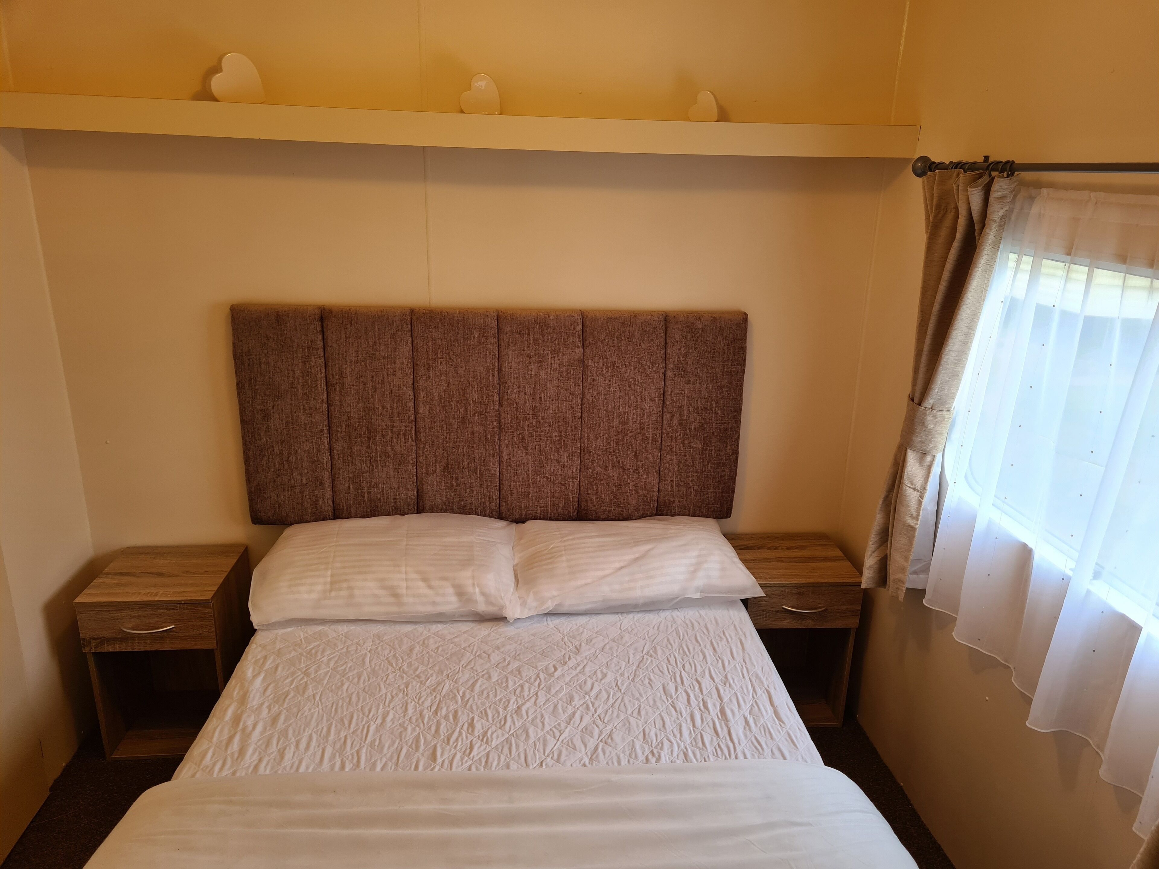 A hotel room with a large bed, wooden nightstands, a headboard, and a window with curtains.