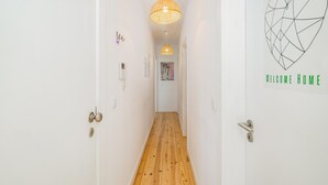 Un pasillo con piso de madera, paredes blancas, un aplique colgante y un letrero que dice 'WELCOME HOME' con un diseño geométrico.