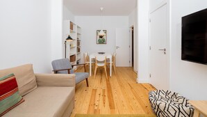 Una sala de estar con un sofá, una mesa de comedor con sillas, una estantería y un televisor montado en la pared.