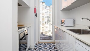 Cocina estrecha con horno empotrado, microondas y lavabo. Una ventana ofrece vistas a un edificio residencial.
