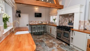 A modern kitchen with a wooden ceiling, a large stove, and a bar area with stools. - The Stables and West Wing (York)