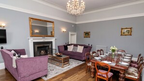 A living room with a fireplace, purple sofas, a dining table set for six, and a chandelier. - The Stables and West Wing (York)