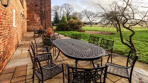 A patio with a brick wall, a large table, and chairs. - The Stables and West Wing (York)