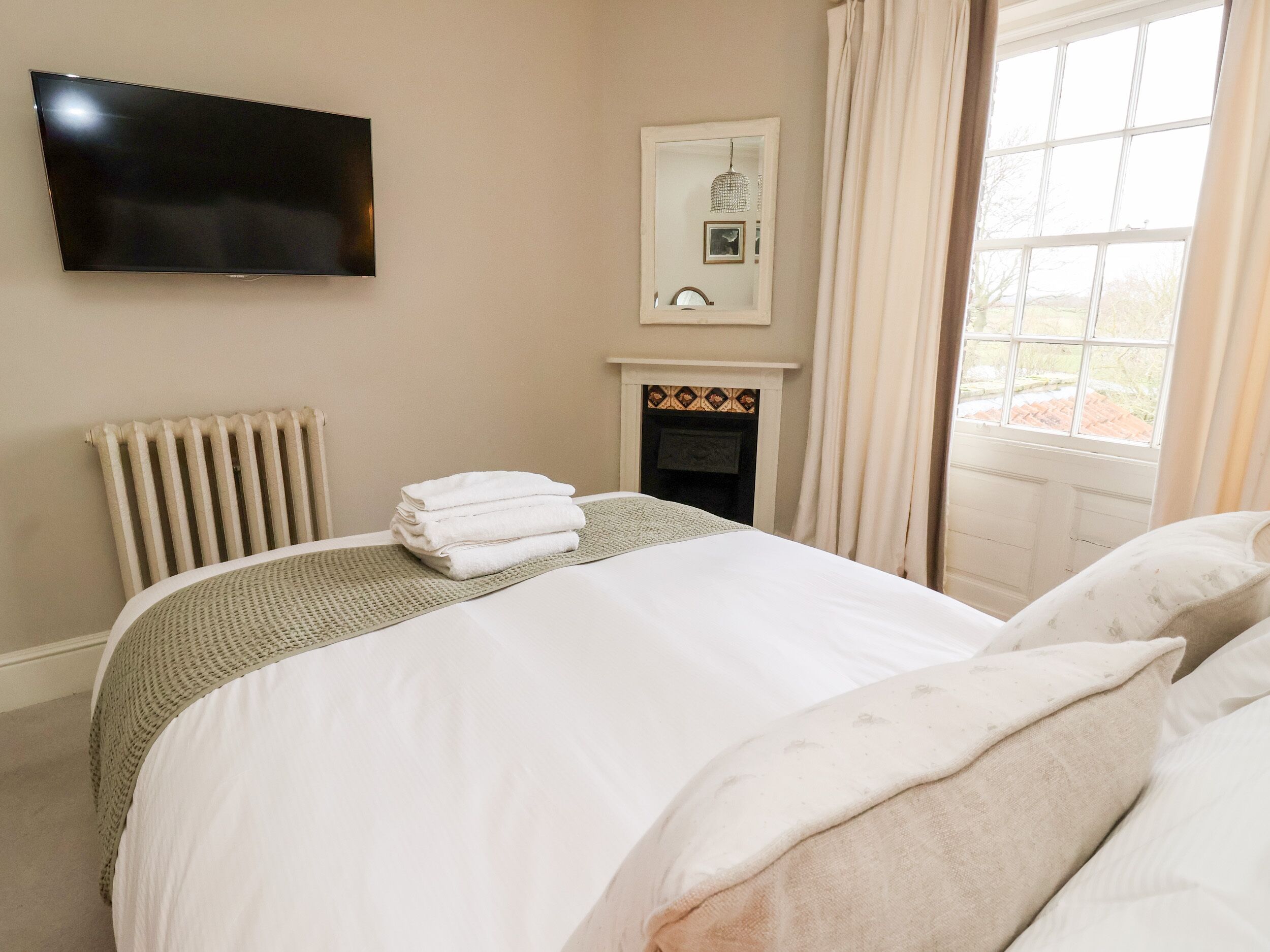 A hotel room with a bed, a flat-screen TV mounted on the wall, a fireplace, and a window with curtains.