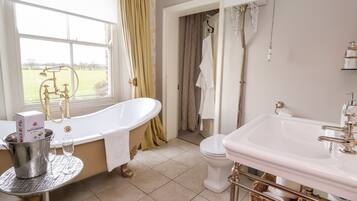 A bathroom with a freestanding bathtub, a white sink with gold fixtures, and a window with curtains.