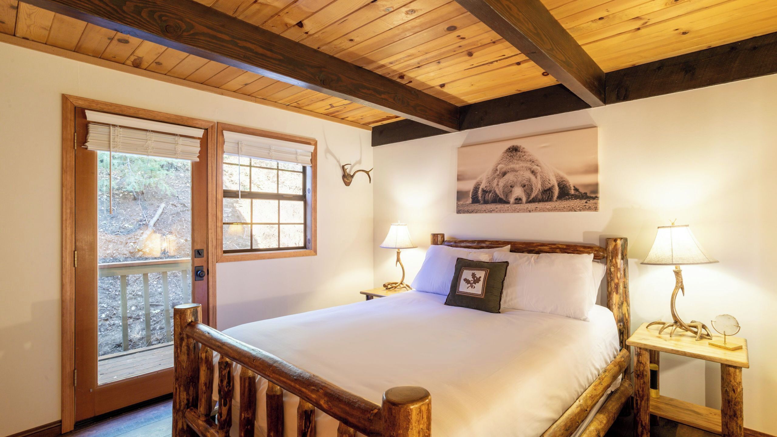 A wooden-framed bed with white bedding, two bedside lamps, a framed bear picture, and a wooden headboard.
