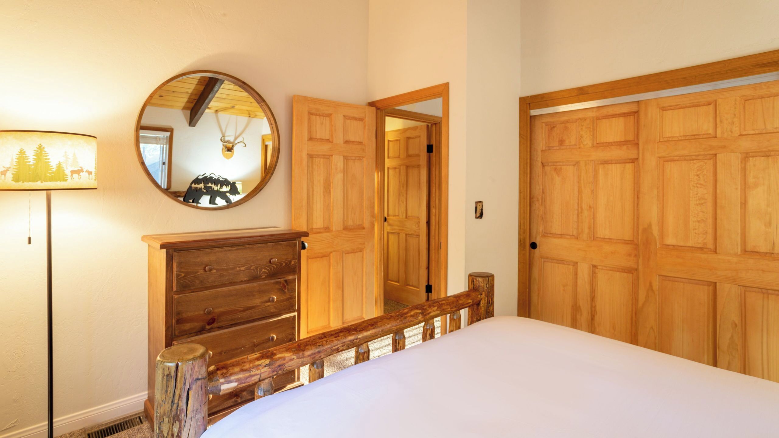 A bedroom with a wooden bed, a round mirror, a lamp, and wooden doors.