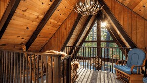 Un intérieur en bois avec un plafond en pente, un lustre, une fenêtre donnant sur des arbres et une chaise bleue.
