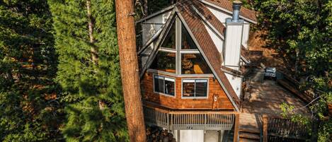 A cabin with a wooden deck, a chimney, and a large window.