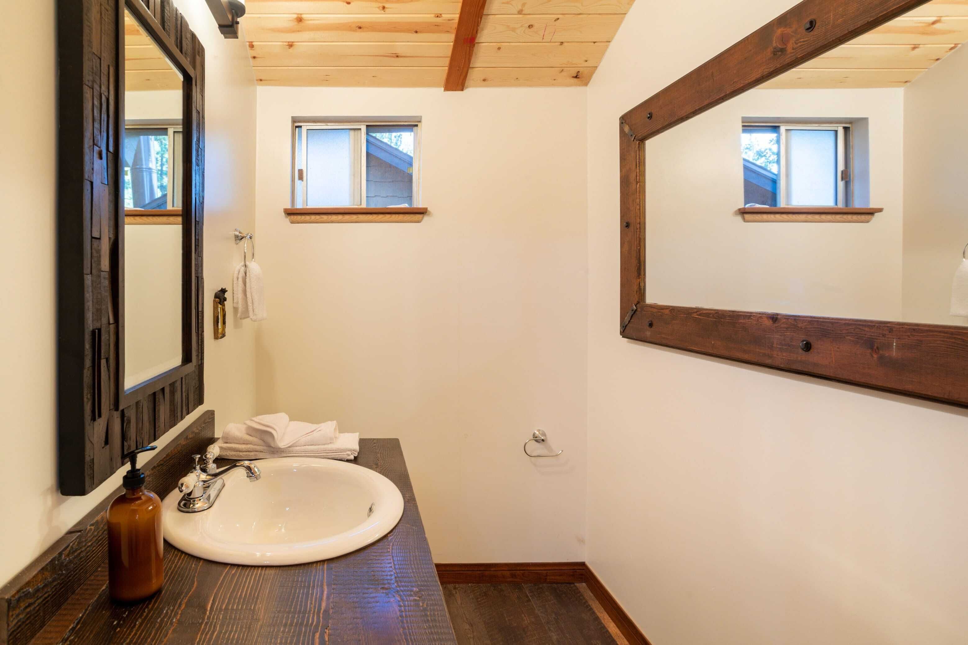 A bathroom with a wooden ceiling, a white sink, a mirror, and two small windows.