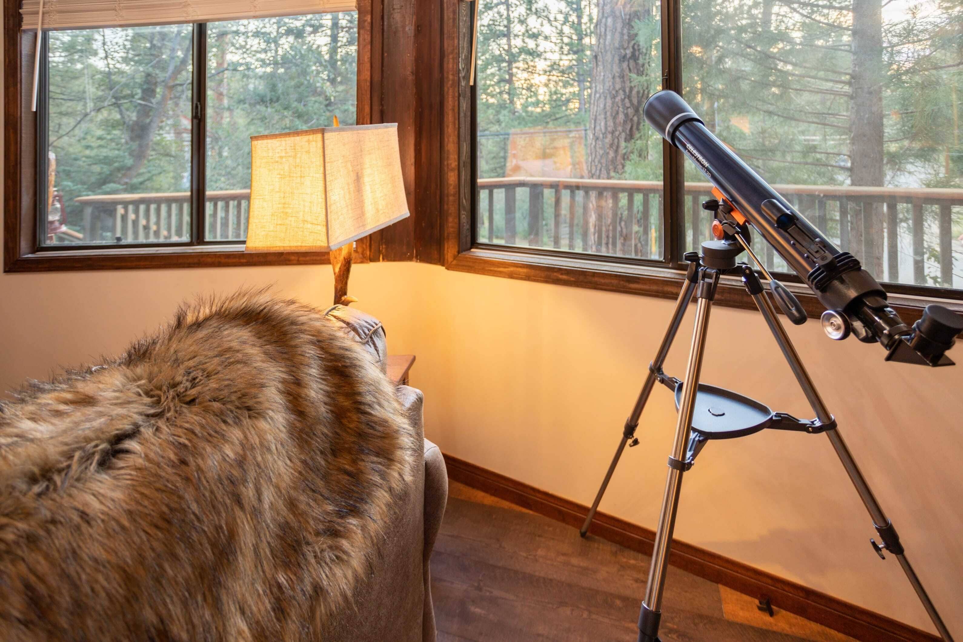 A room with a telescope on a tripod, a lamp, and a view of a deck with a railing.