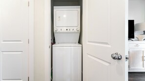 A laundry room with a washer and dryer, a cabinet with a television, and a door with a silver handle.