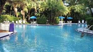A swimming pool with lounge chairs and umbrellas, surrounded by greenery.