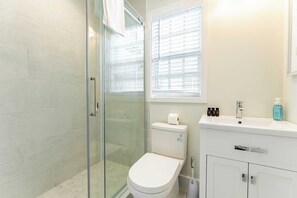 A modern bathroom with a glass shower enclosure, a toilet, and a sink with toiletries.