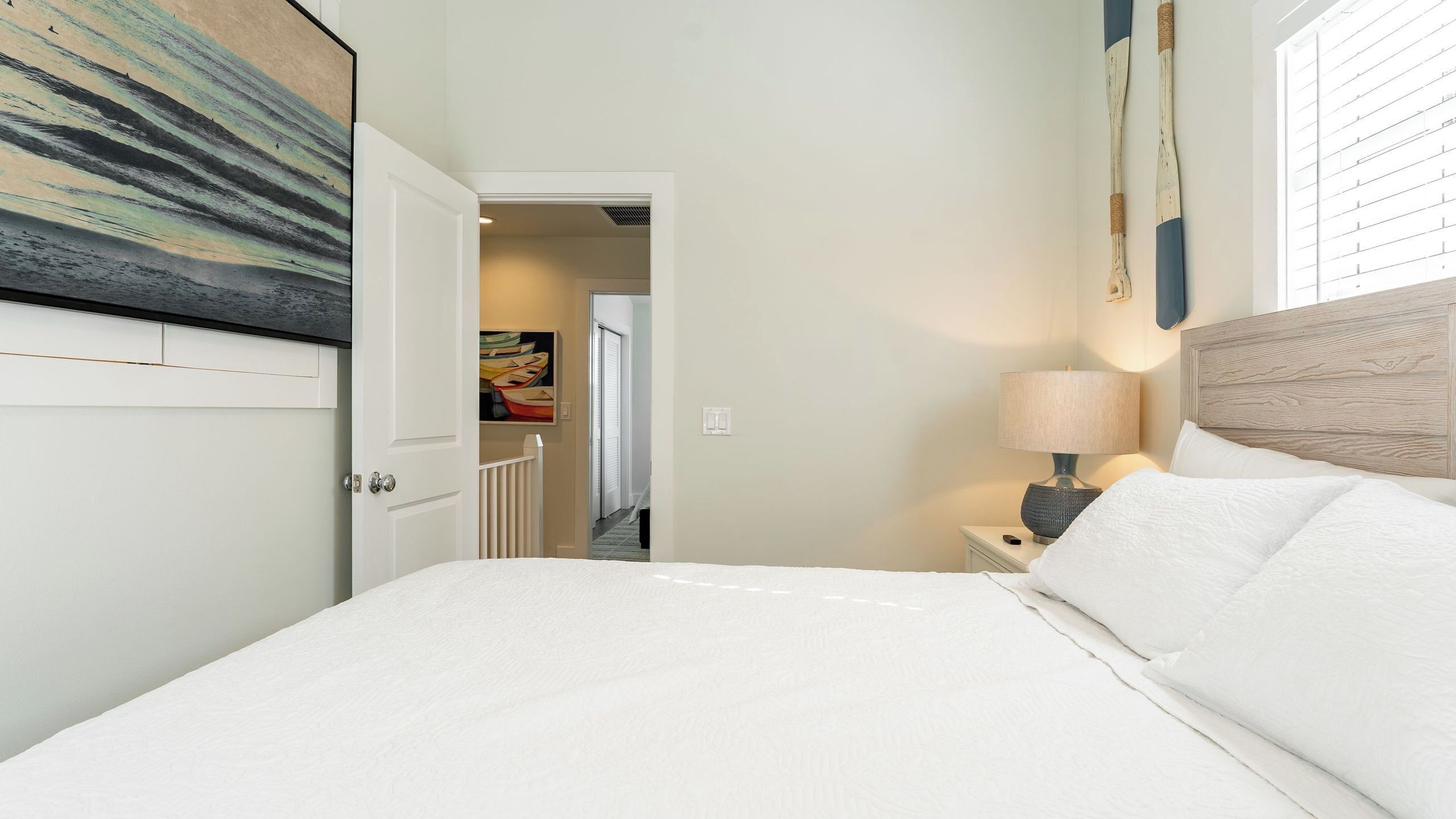 Habitació d'hotel amb un llit, una tauleta de nit amb una làmpada, una porta que dona a un passadís i un quadre a la paret.