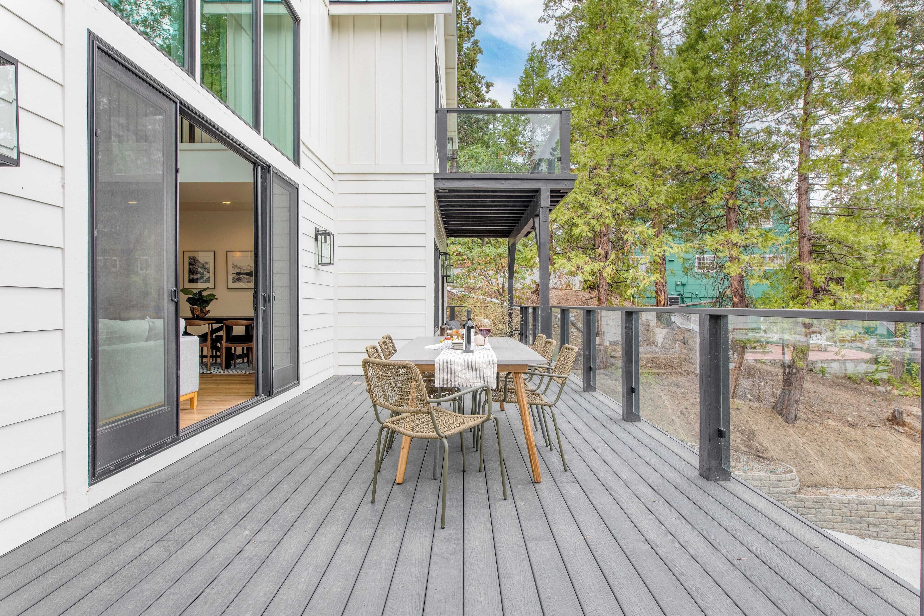 Une terrasse extérieure avec une table et des chaises, une porte vitrée donnant sur une pièce, et une vue sur une zone boisée.